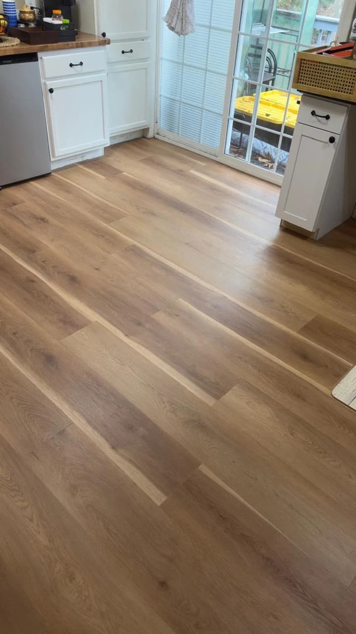 Warm wide-plank flooring beside white kitchen cabinets