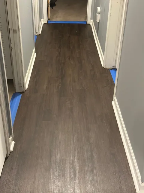 Dark plank flooring along a hallway with white trim