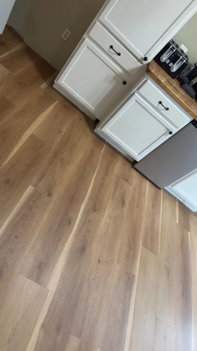 Warm wide-plank flooring beside white kitchen cabinets